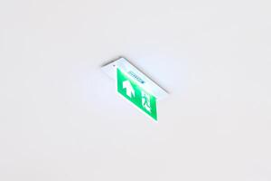 White neon sign depicting a fire exit with green background hangs from the ceiling. photo