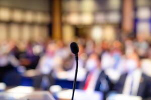 Small microphone behind the podium for the MC, master of ceremony, with a blurry crowd audience in the background in a seminar. photo