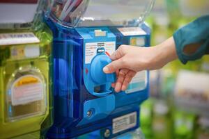 A human hand in a turquoise sweater is twisting a blue gashapon machine to release a figure. In Japan, it is considered as one of the most well liked risks. photo