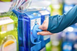 A human hand in a turquoise sweater is twisting a blue gashapon machine to release a figure. In Japan, it is considered as one of the most well liked risks. photo