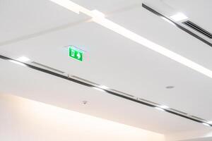 White neon sign depicting a fire exit with green background hangs from the ceiling. photo
