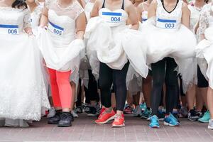 Crowd of brides prepares for their race by lining up in front of starting line, in which groom will serve as their goal. It's a Start of Love Story. photo