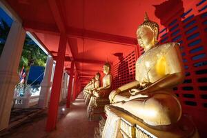 Several golden statues of Buddha statues in meditation posture are lined up in a corridor and spotlight on every statues in front of the red wall. photo