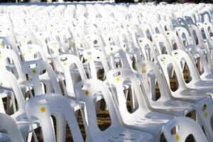Many white plastic chairs were set up in a square area with the row and column for outdoor concerts or open air events. photo