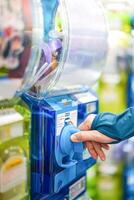 A human hand in a turquoise sweater is twisting a blue gashapon machine to release a figure. In Japan, it is considered as one of the most well liked risks. photo