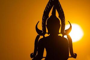 Silhouette Buddha statue between creating and building process, at outdoor field with the sun set and twilight period time., Thailand. photo