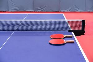 Two pingpong table tennis rackets for playing are laid on next to net on the blue table. This is one of ping pong sports equipment for players. photo