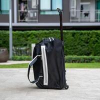A traveler's black and white stripe suitcase with wheels was left alone on the footpath with the blurred bushes background of a luxury condo. photo