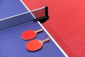 Two pingpong table tennis rackets for playing are laid on next to net on the blue table. This is one of ping pong sports equipment for players. photo