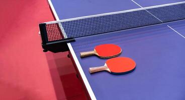 Two pingpong table tennis rackets for playing are laid on next to net on the blue table. This is one of ping pong sports equipment for players. photo