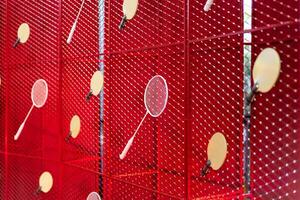 Table tennis and badminton rackets are hung on a red square grill steel grid, used as a backdrop for various events. photo