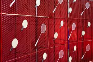 Table tennis and badminton rackets are hung on a red square grill steel grid, used as a backdrop for various events. photo