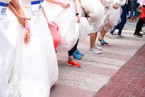 Crowd of brides prepares for their race by lining up in front of starting line, in which groom will serve as their goal. It's a Start of Love Story. photo