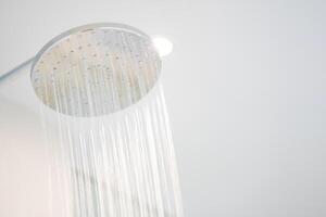 Water was pouring out from a large circular shower in the dimly lit bathroom that has a glass window and can see the view outside. photo