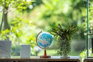 A miniature replica of the globe is placed on wooden table beside bookshelf in the library. photo