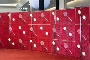 Table tennis and badminton rackets are hung on a red square grill steel grid, used as a backdrop for various events. photo