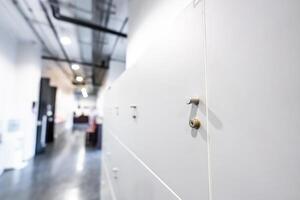 Large gray locker with each locker closed located beside corridors inside building are dimly lit. photo