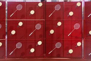 Table tennis and badminton rackets are hung on a red square grill steel grid, used as a backdrop for various events. photo