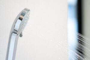 Water was pouring out from a large circular shower in the dimly lit bathroom that has a glass window and can see the view outside. photo