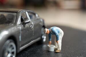 Miniature people, A worker bends over as if inspecting or repairing something on a sleek metallic gray car model photo