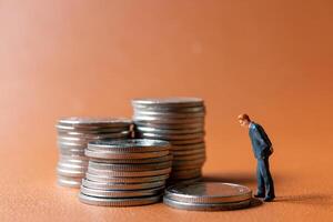 Miniature people A businessman in a suit stands with several stacks of silver coins photo
