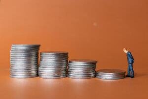 Miniature people A businessman in a suit stands with several stacks of silver coins photo