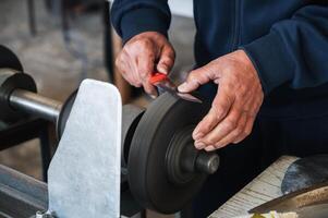 male sharpener grinder sharpens knife blade on sharpening machine with rotating abrasive wheel close-up photo