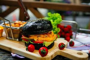 Black Burger With Fries and Tomatoes on Wooden Board photo