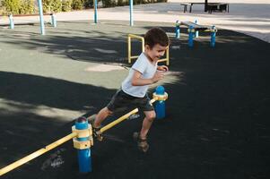 preschool child boy plays on horizontal bars on playground in park in summer photo