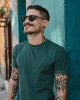 A man wearing a green t-shirt smiles while leaning against a wall photo