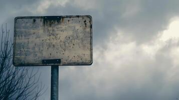 A weathered sign stands tall against a cloudy sky photo
