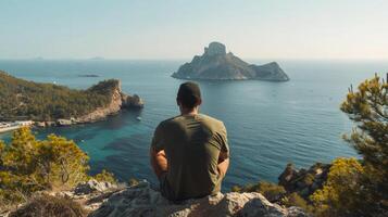 A man sits on a cliff overlooking the turquoise waters of Ibiza photo