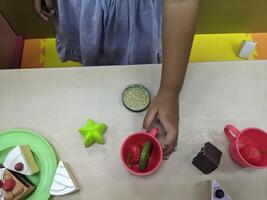 Child Playing with Play Food. A young child playing with plastic toy food, setting a table with cakes and fruit. photo