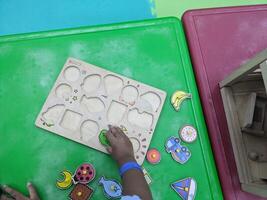 Child Playing with Wooden Puzzles. A young child playing with wooden puzzles on a green table. The puzzles are colorful and feature various shapes, encouraging creativity and learning. photo