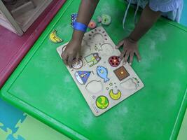 Child Playing with Wooden Puzzles. A young child playing with wooden puzzles on a green table. The puzzles are colorful and feature various shapes, encouraging creativity and learning. photo