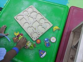 Child Playing with Wooden Puzzles. A young child playing with wooden puzzles on a green table. The puzzles are colorful and feature various shapes, encouraging creativity and learning. photo