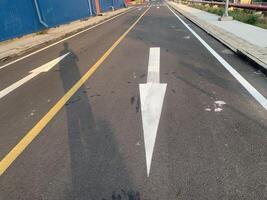 Road Marking with a White Arrow. A close-up view of white painted arrows on a grey asphalt road. The arrows indicate direction and guidance for vehicles. photo