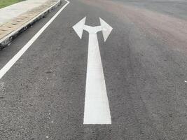 Road Marking with a White Arrow. A close-up view of white painted arrows on a grey asphalt road. The arrows indicate direction and guidance for vehicles. photo