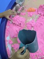 Child Playing with Pink Sand in a Sensory Table.A young child's hand reaches into a sensory table filled with pink sand. Toys are visible surrounding the table, adding to the playful atmosphere. photo