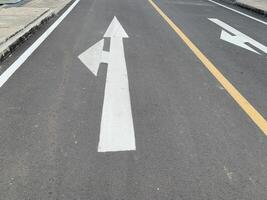 Road Marking with a White Arrow. A close-up view of white painted arrows on a grey asphalt road. The arrows indicate direction and guidance for vehicles. photo