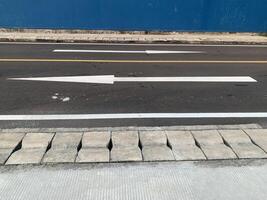 Road Marking with a White Arrow. A close-up view of white painted arrows on a grey asphalt road. The arrows indicate direction and guidance for vehicles. photo
