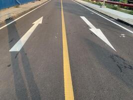 Road Marking with a White Arrow. A close-up view of white painted arrows on a grey asphalt road. The arrows indicate direction and guidance for vehicles. photo