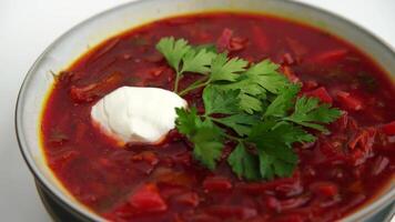 A bowl of of borscht red soup with a green leaf on top. The soup is garnished with a dollop of sour cream. video