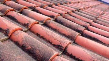 Closeup of red tiles on roof of an old house. The tile pattern shows weathered texture and age. This highlights the craftsmanship and details of tile roofing in traditional architecture video