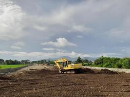 West Lombok Regency, Indonesia - February 4, 2024. Outdoors, a Backhoe is at work leveling the ground for a housing site, with a blue sky in the background. photo