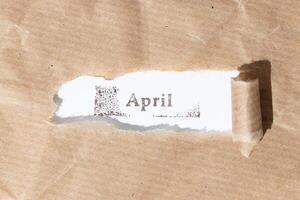 Brown paper torn stripe with ink stamp text April on white paper background photo