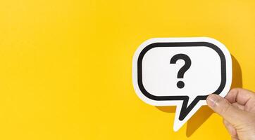 Hand holding a question mark on speech bubble on yellow background. Copy space photo
