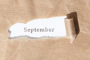 Brown paper torn stripe with ink stamp text September on white paper background photo