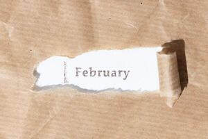 Brown paper torn stripe with ink stamp text February on white paper background photo