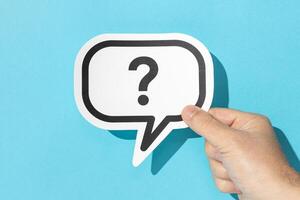 Hand holding a question mark on speech bubble on blue background. Doubt, confusion, uncertainty concept photo